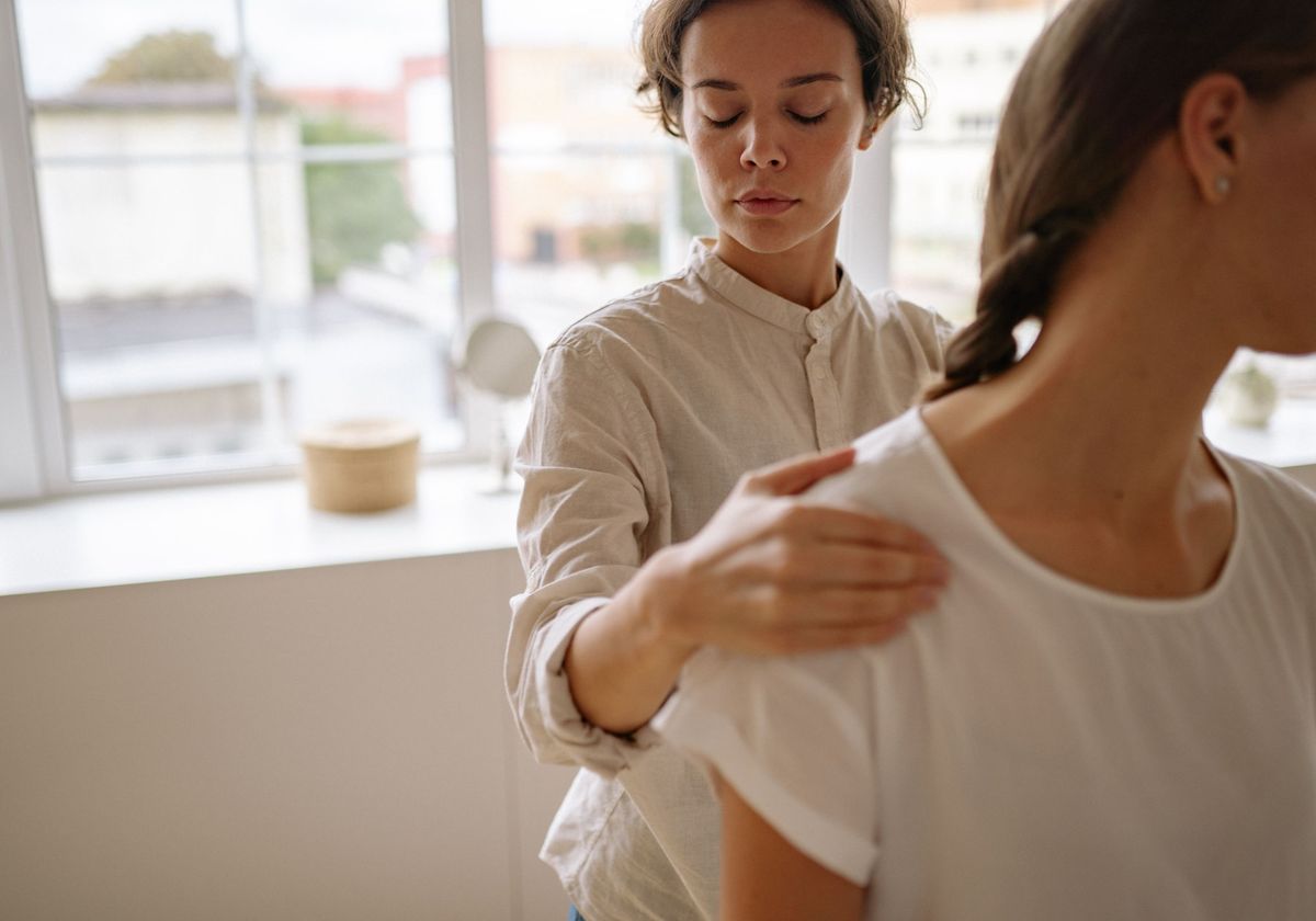 A physical therapist working on a patient’s shoulder in a sunlit clinic